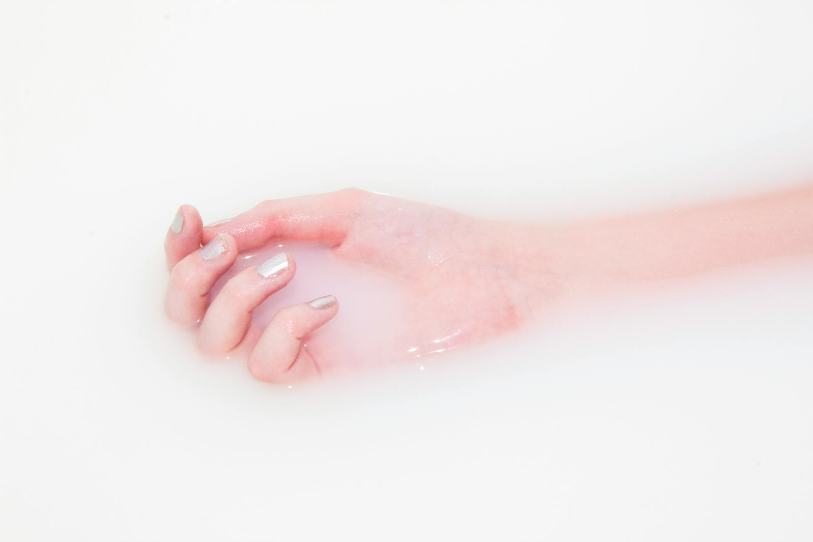 A woman's manicured hand soaks in milky water, creating a minimalist and soothing texture.
