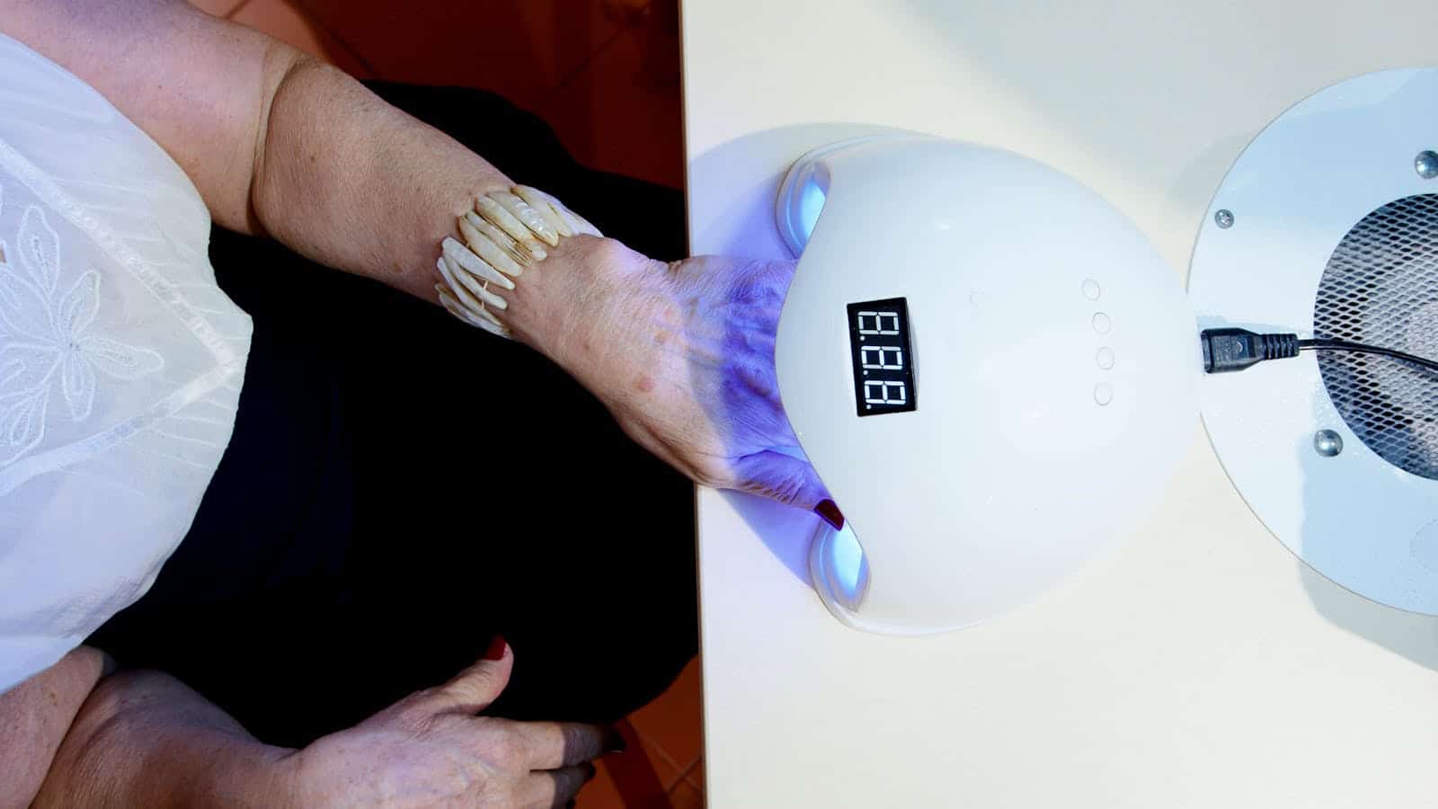 Close-up of a woman's hand with a bracelet using a nail dryer in a salon setting.