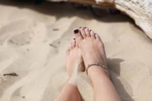 Close-up of feet in sand wearing an anklet, capturing the essence of a summer day at the beach.
