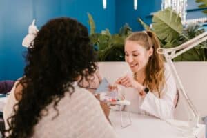 Manicurist assisting a client in a modern nail salon with vibrant indoor decor.